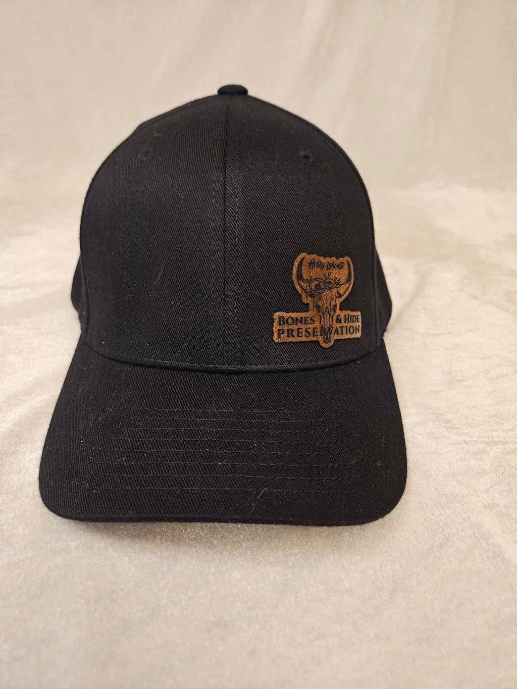 Black cap with engraved leather Bones & Hide Preservation patch, front