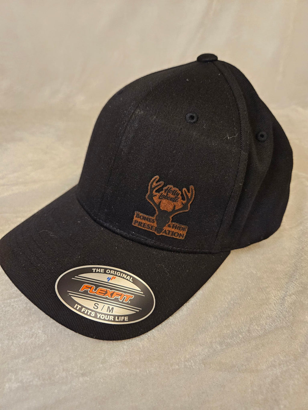 Men's black stretch hat with engraved leather Bones & Hide Preservation patch, angled