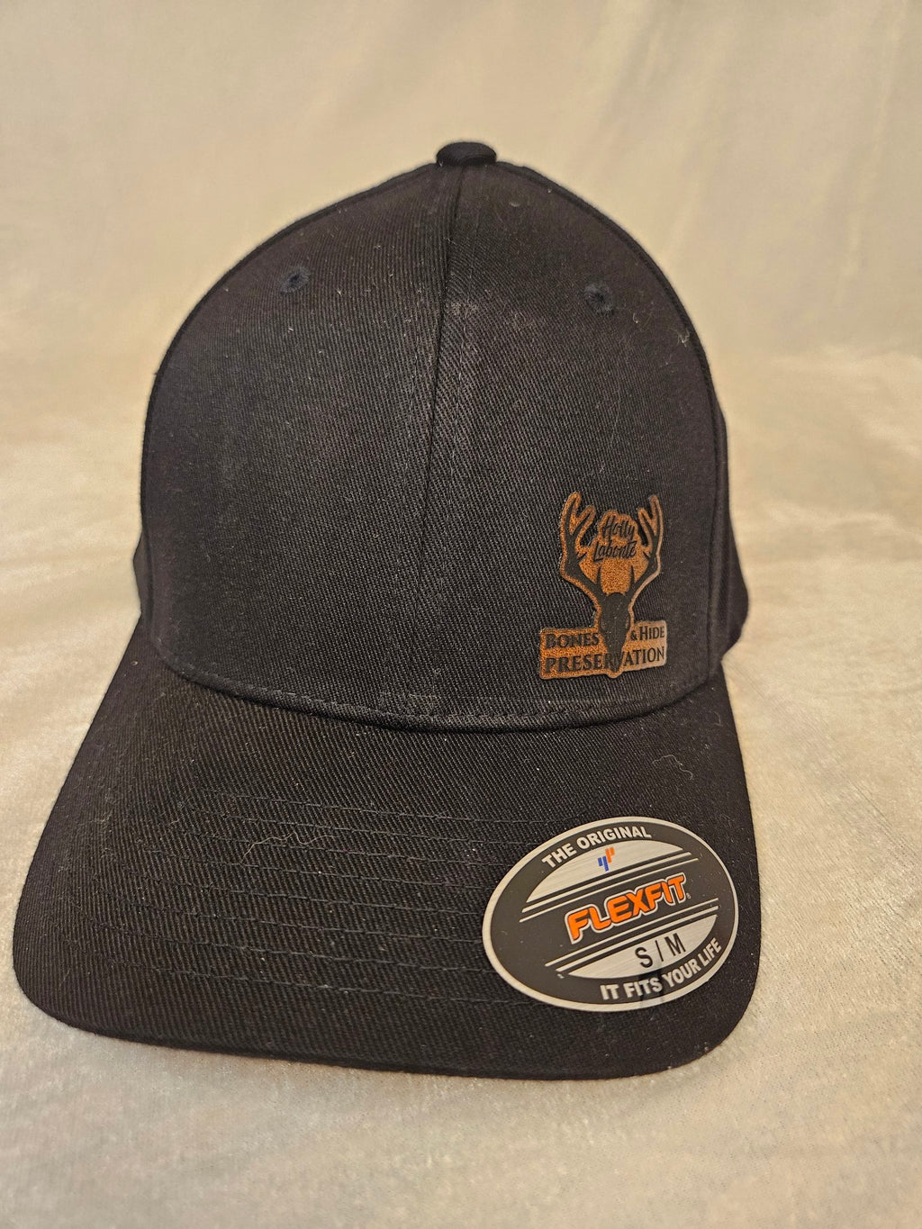 Men's black stretch hat with engraved leather Bones & Hide Preservation patch, front