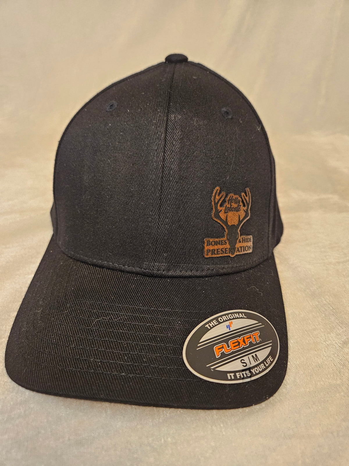 Men's black stretch hat with engraved leather Bones & Hide Preservation patch, front