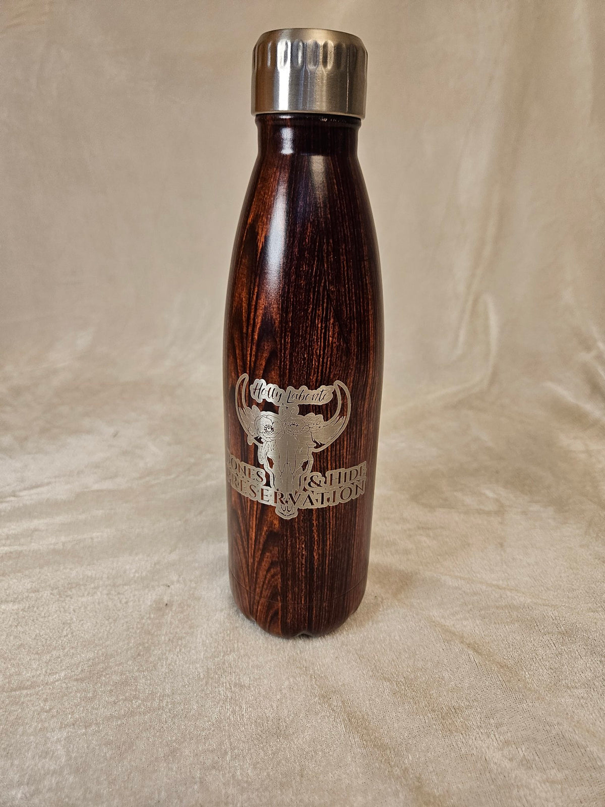 Wood-grain water bottle with engraved female Bones & Hide Preservation logo, front