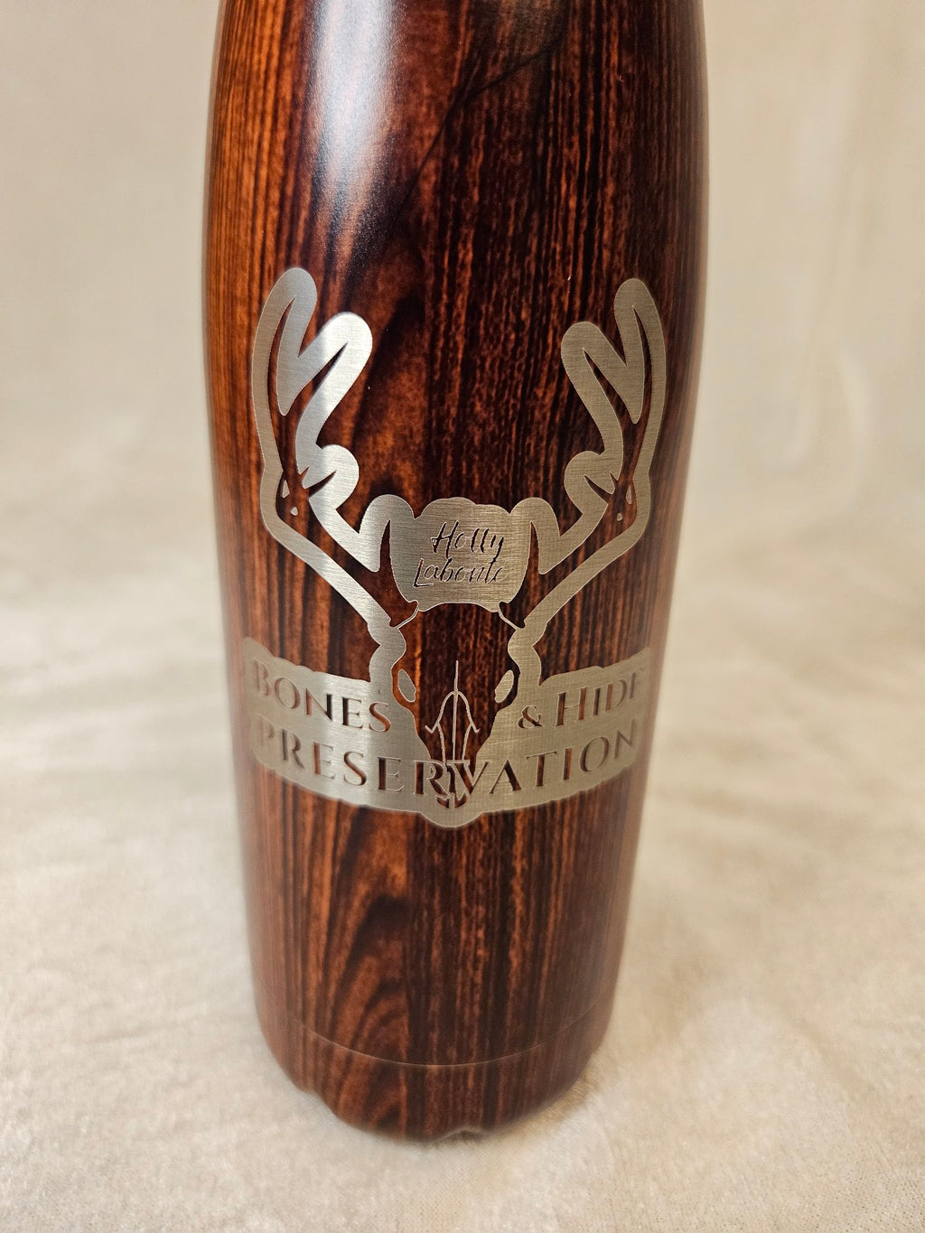Close-up of engraved male antler logo on wood-grain water bottle