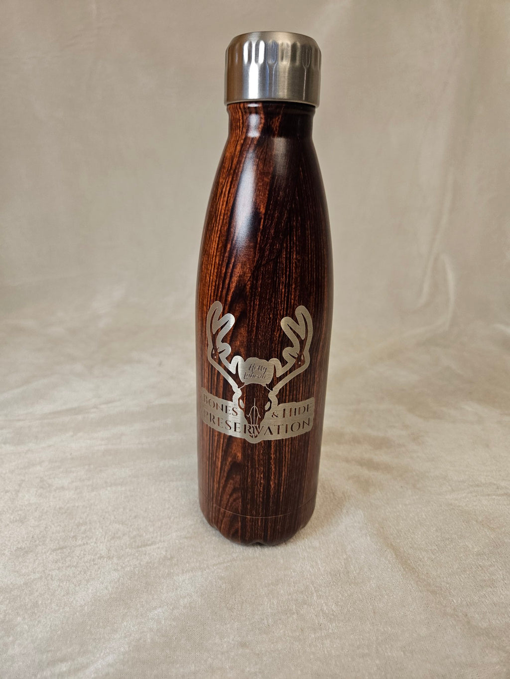 Wood-grain water bottle with engraved male antler Bones & Hide Preservation logo, front